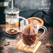 Delicious french press coffee in a glass mug, placed on a wooden coaster.
