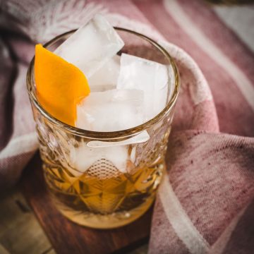 Gorgous glass filled with a delicious old fashioned drink. Placed on wooden coaster.