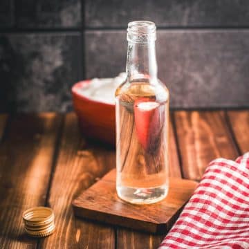 Gorgous preserving bottle, filled with sugar syrup on wooden coaster. A heart shaped bowl, filled with granulated sugar is reflected in the bottle.