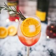 Gorgeous wine glass filled with Winter Aperol spritz, placed on snowy ground.