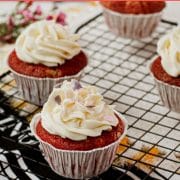 Cream cheese frosting with heart shaped sprinkles on top of red velvet muffin.