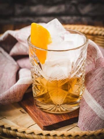 Gorgous glass filled with a delicious old fashioned drink. Placed on wooden coaster.