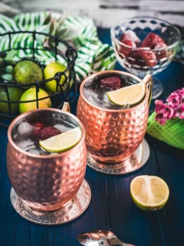 Gorgeous copper cups filled with delicious strawberry Moscow mule placed on blue wooden ground.