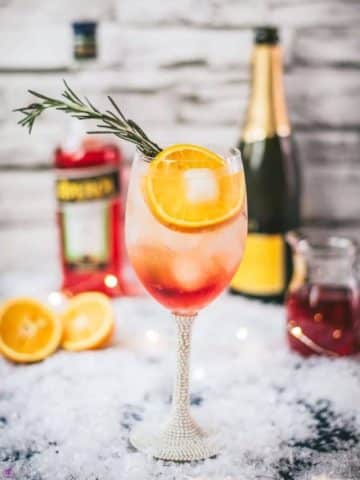 Gorgeous wine glass filled with Winter Aperol spritz, placed on snowy ground.