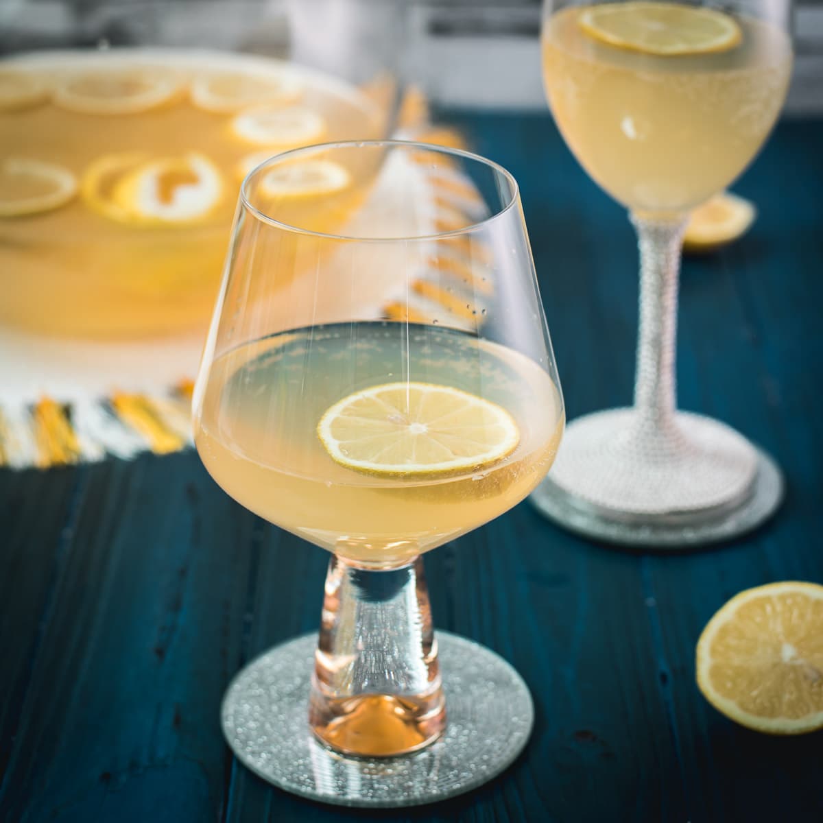 Two glassed filled with lemon punch. Garnished with a lemon slice and placed on a mirror coaster.