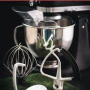 Matt black Kitchenaid stand mixer with various accessories placed on a green felt mat.