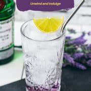 Highball glass filled with lavender gin and tonic, garnished with lime wedge and straw. Placed on black slate plate.