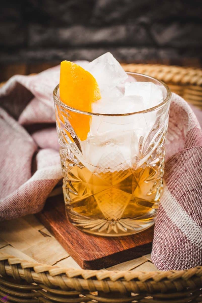 Gorgous glass filled with a delicious old fashioned drink. Placed on wooden coaster.