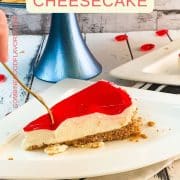 A slice of delicious Valentine's Raspberry Cheesecake placed on white plate next to a golden fork .