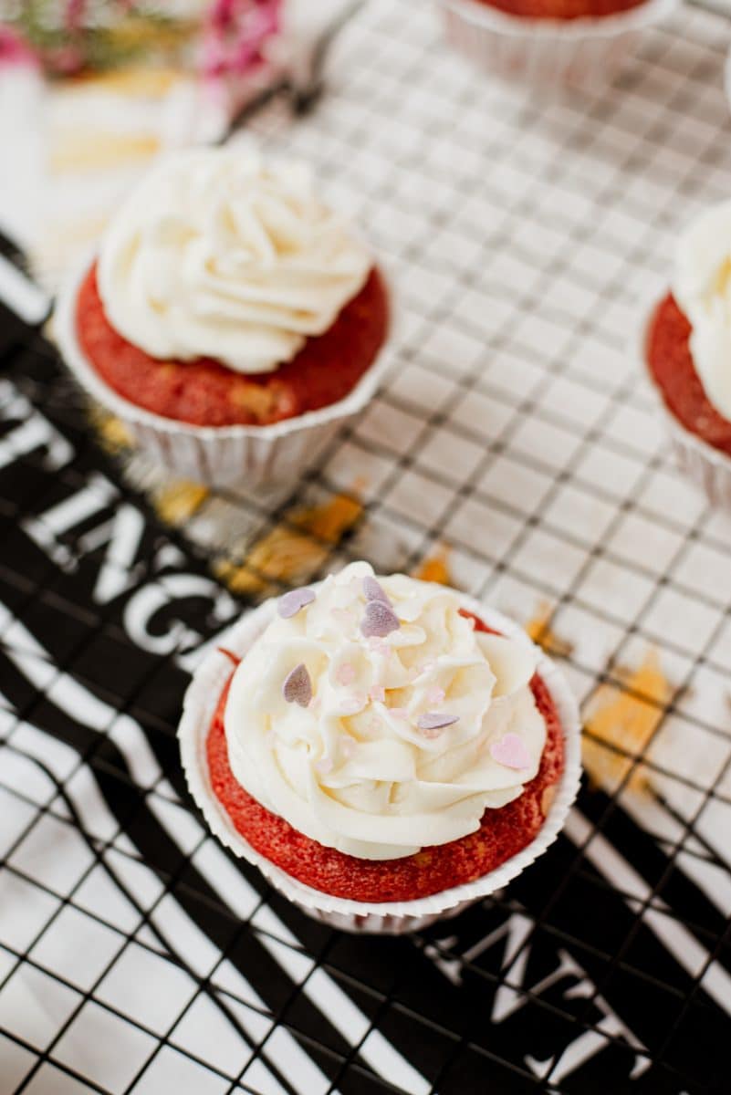 Cream cheese frosting with heart shaped sprinkles on top of red velvet muffin.