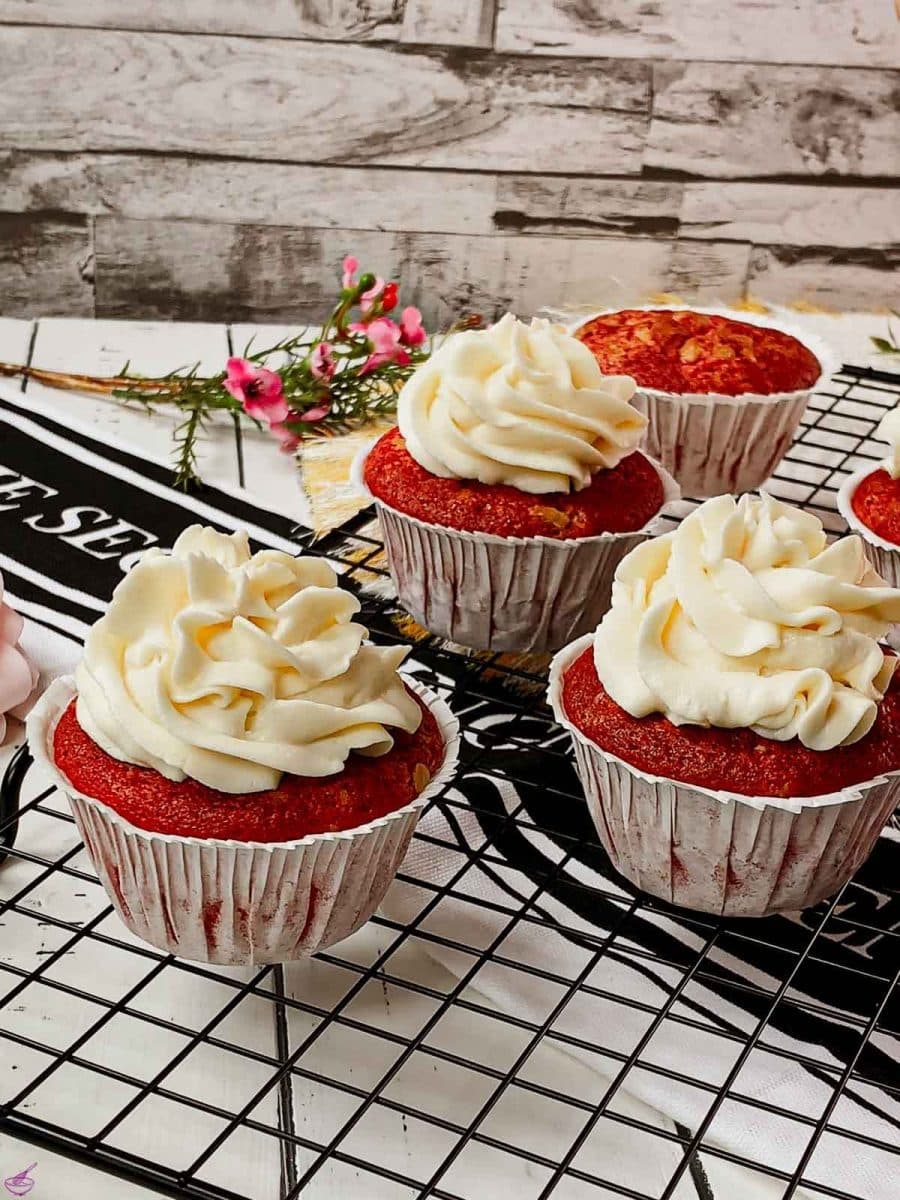 Cream cheese frosting on top of red velvet muffin placed on cooling rack.