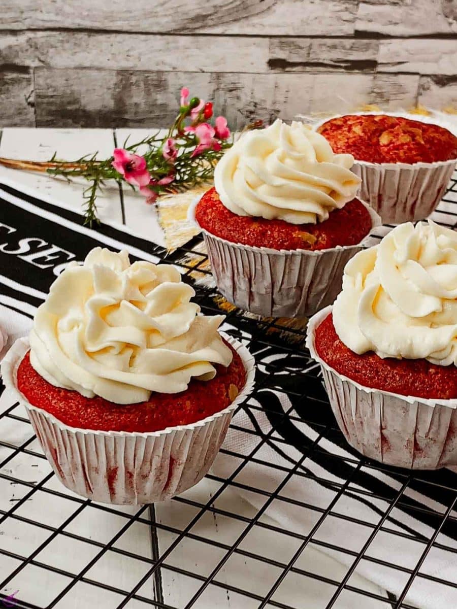 Cream cheese frosting on top of red velvet muffin placed on cooling rack.