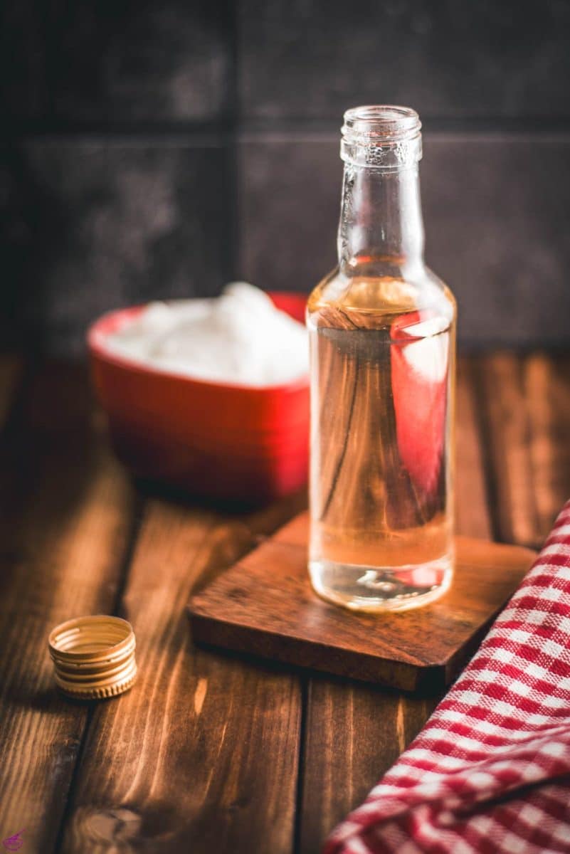 Gorgous preserving bottle, filled with sugar syrup on wooden coaster. A heart shaped bowl, filled with granulated sugar is reflected in the bottle.