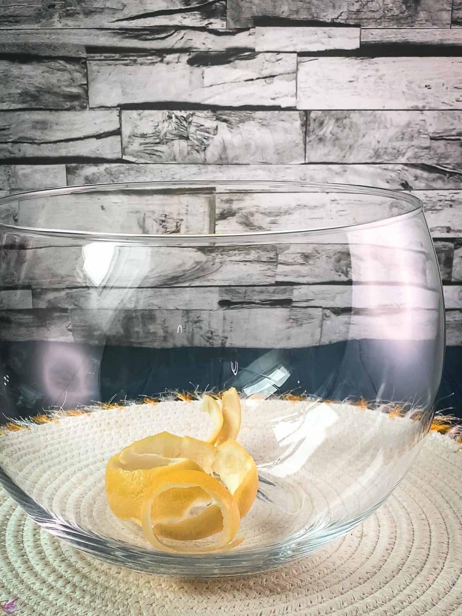 Glass punch bowl, placed on white table mat filled with lemon zest.