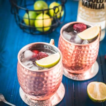 Gorgeous copper cups filled with delicious strawberry Moscow mule placed on blue wooden ground.