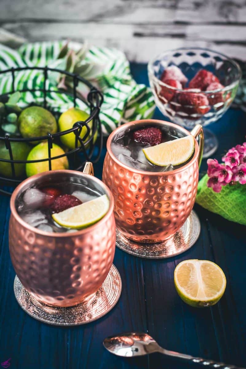 Gorgeous copper cups filled with delicious strawberry Moscow mule placed on blue wooden ground.