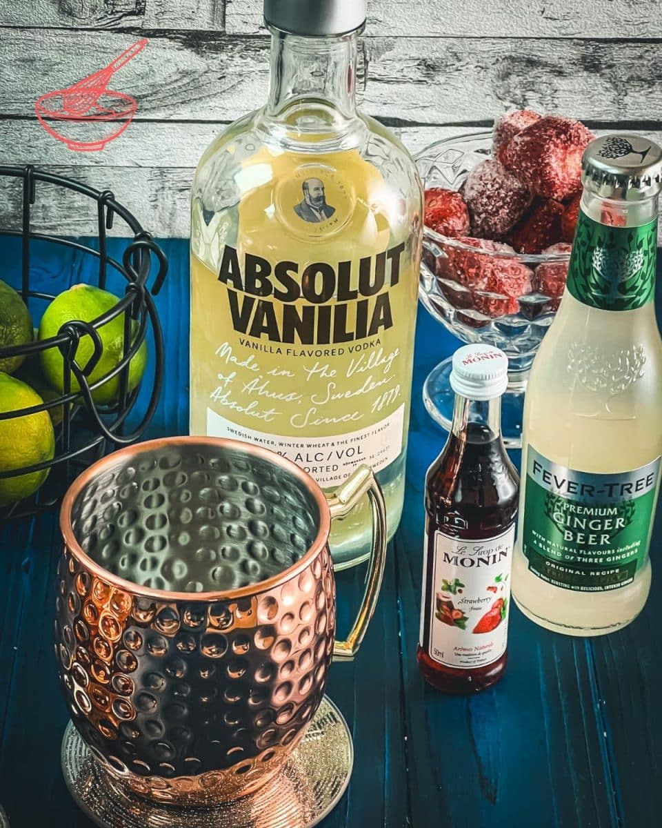 Ingredients for making a delicious strawberry Moscow mule - lime juice, ginger beer, vanilla vodka, strawberry syrup.