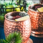 Gorgeous copper cups filled with delicious strawberry Moscow mule placed on blue wooden ground.