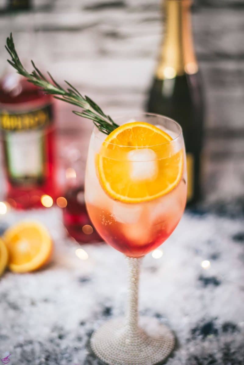 Gorgeous wine glass filled with Winter Aperol spritz, placed on snowy ground.