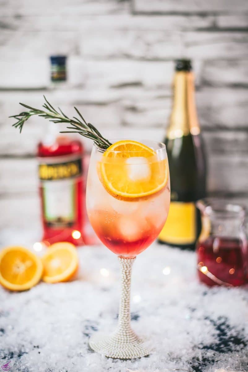 Gorgeous wine glass filled with Winter Aperol spritz, placed on snowy ground.