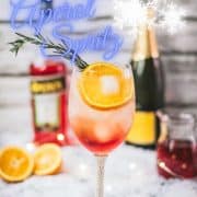 Gorgeous wine glass filled with Winter Aperol spritz, placed on snowy ground.