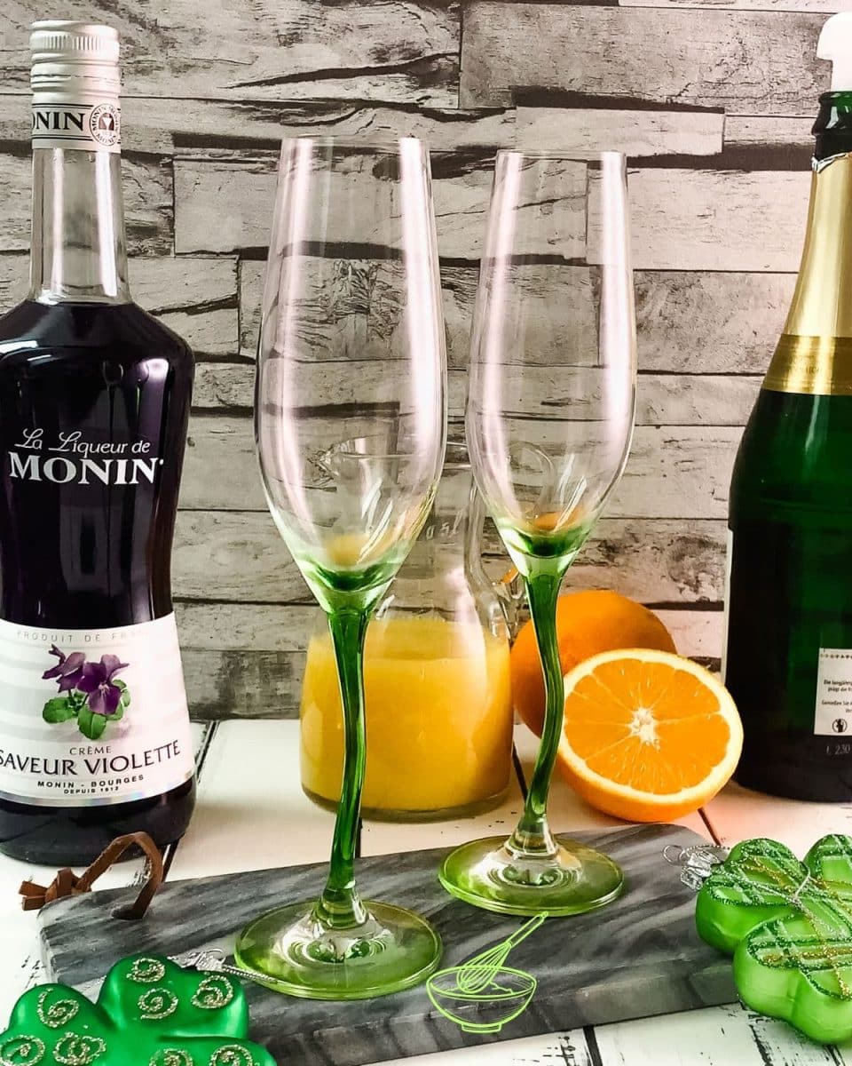 Ingredients for a green mimosa - sparkling wine, orange juice, and violet liqueur.