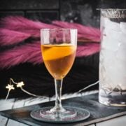 Glass filled with a delicious Martinez cocktail, garnished with a lemon zest. Placed on a black slate.