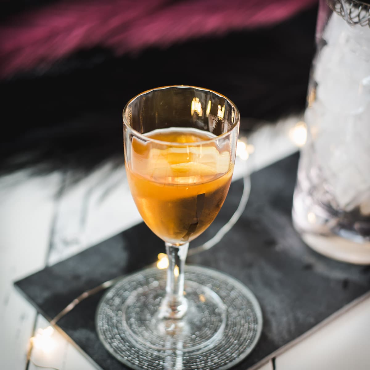 Glass filled with a delicious Martinez cocktail, garnished with a lemon zest. Placed on a black slate.