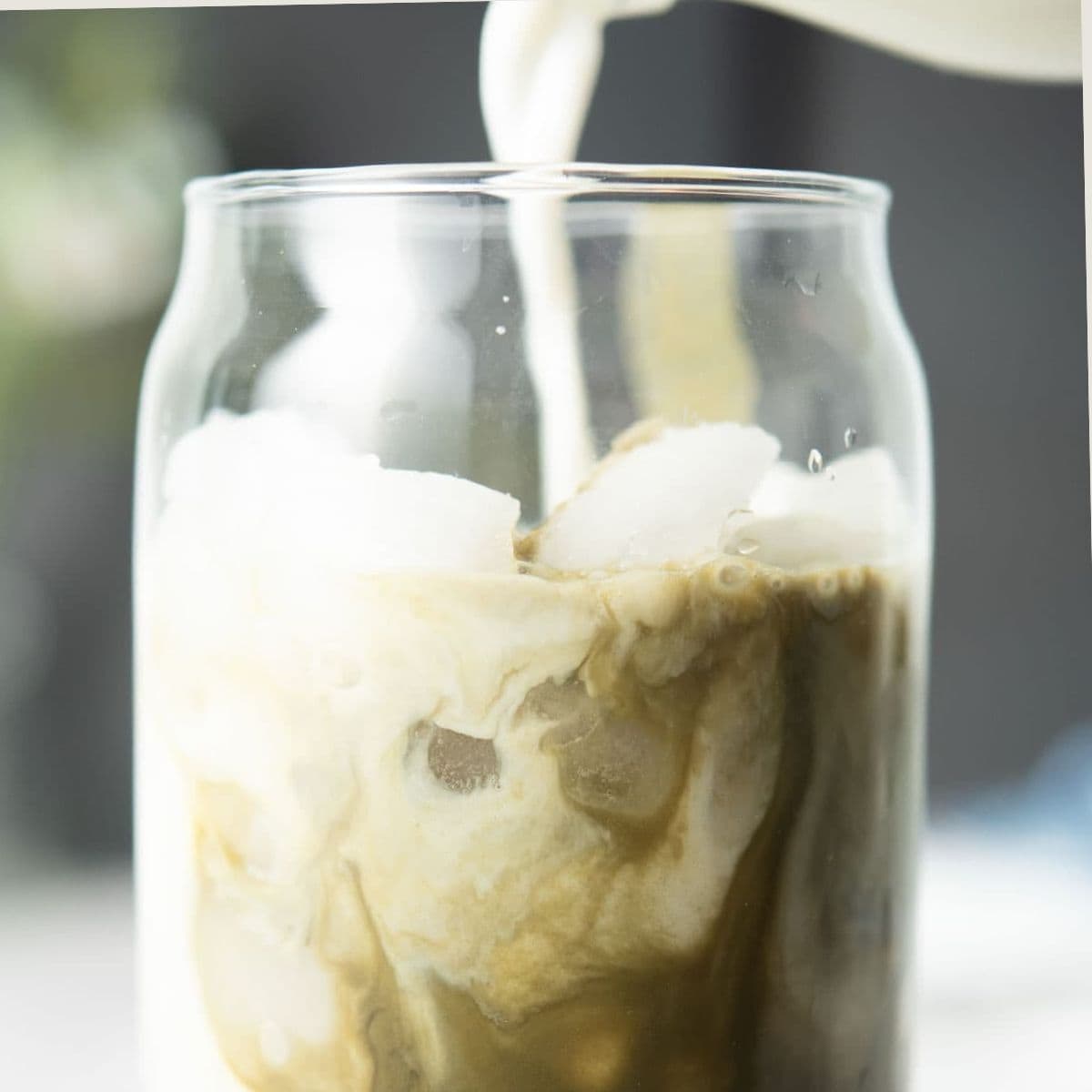 Pouring oat milk into glass with matcha.