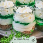 Gorgeous no bake lime cheesecakes in a jar for celebrating St. Patrick's Day! Placed on a white plate sitting on a brown wooden floor.