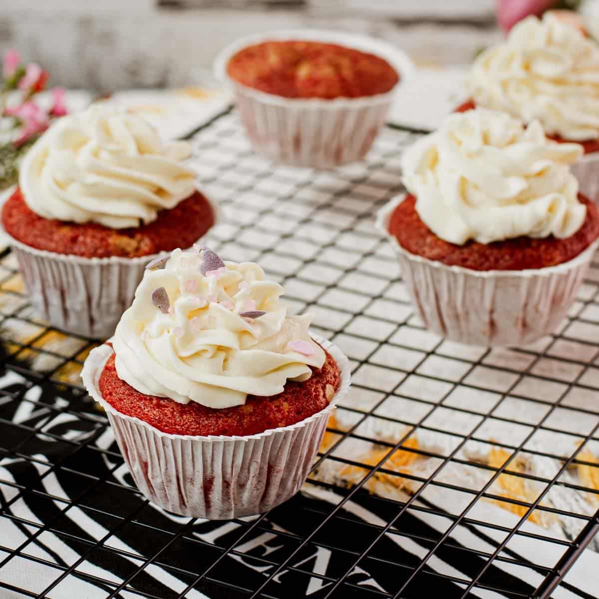 Cream cheese frosting with heart shaped sprinkles on top of red velvet muffin.