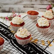 Cream cheese frosting with heart shaped sprinkles on top of red velvet muffin.
