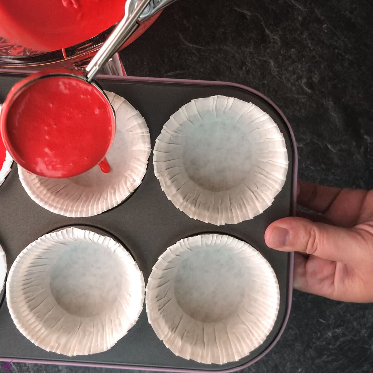 Scooping red velvet dough into muffin tins.