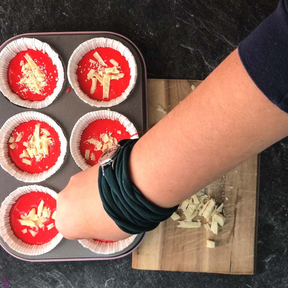 Hand sprinkling chopped white chocolate on red velvet muffin dough.