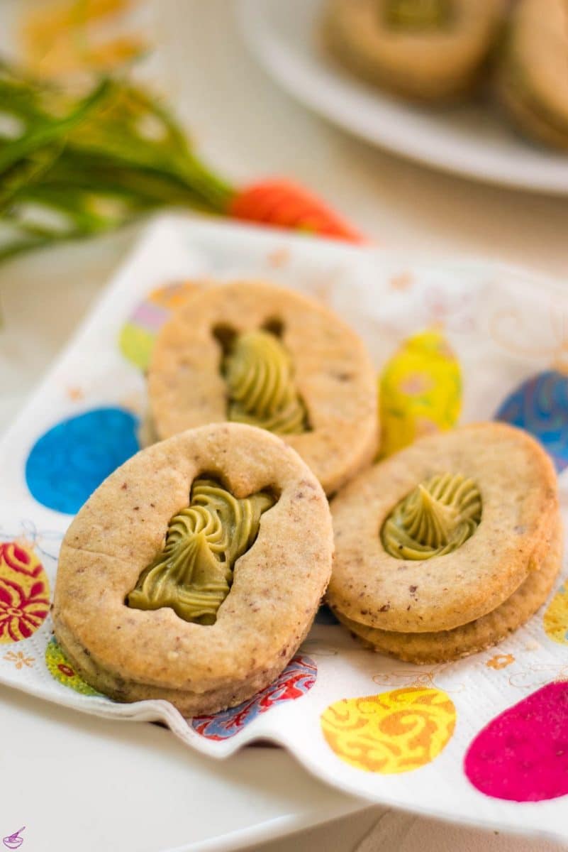 Gorgous cut out Easter cookies with pistachio ganache placed on Easter napkin.