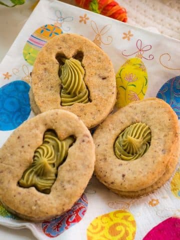 Gorgous cut out Easter cookies with pistachio ganache placed on Easter napkin.