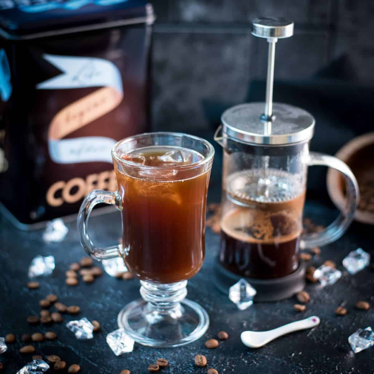 Delicious iced French press coffee served in a gorgeous glass, placed next to a French press.