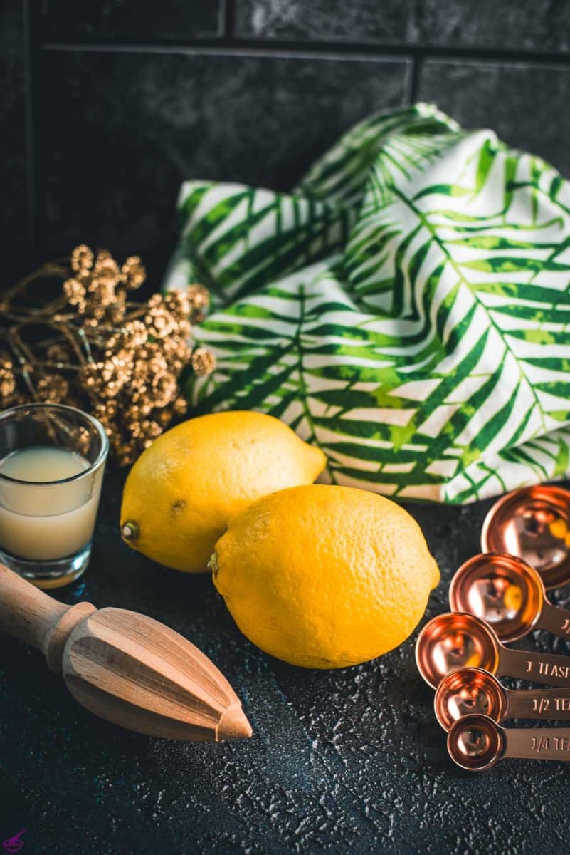 Lemons, placed on dark ground next to lemon juice and lemon squeezer.