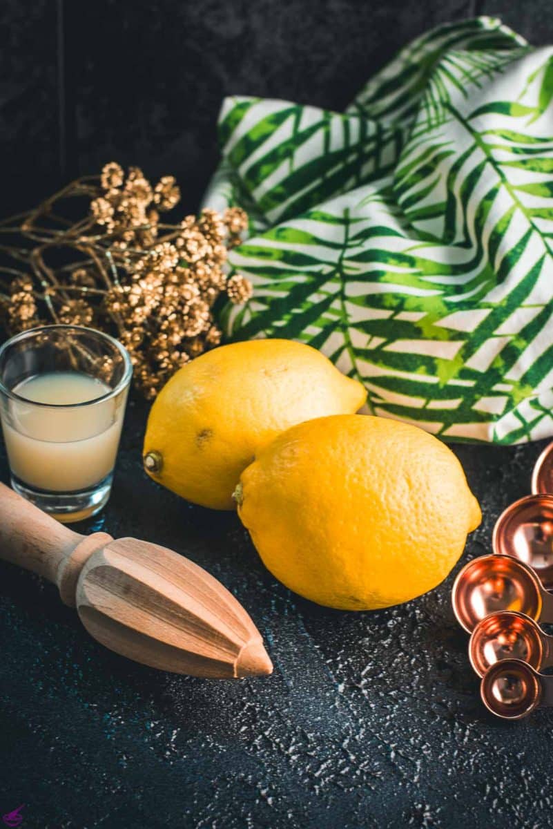 Lemons, placed on dark ground next to lemon juice and lemon squeezer.