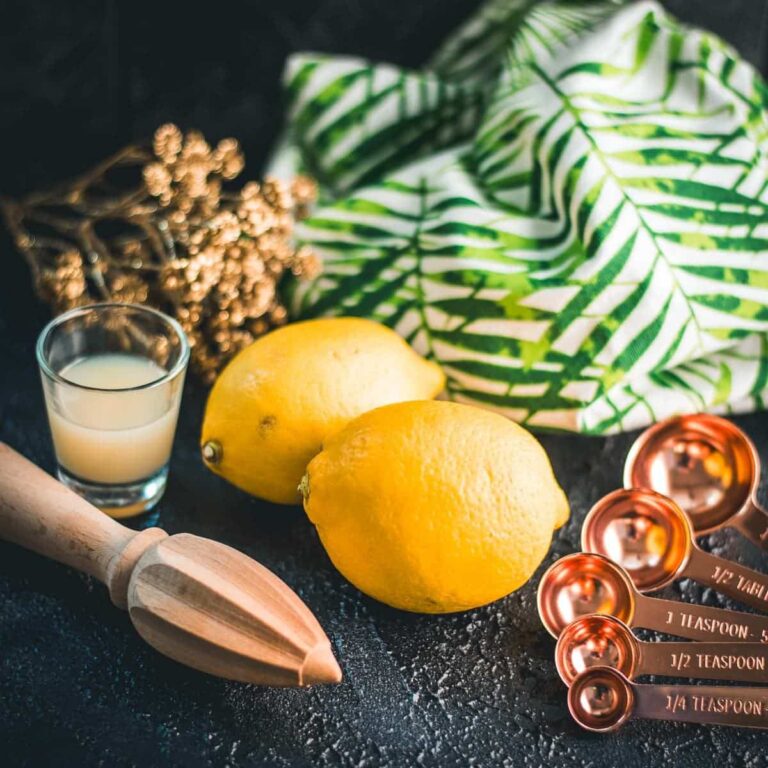 Lemons, placed on dark ground next to lemon juice and lemon squeezer.
