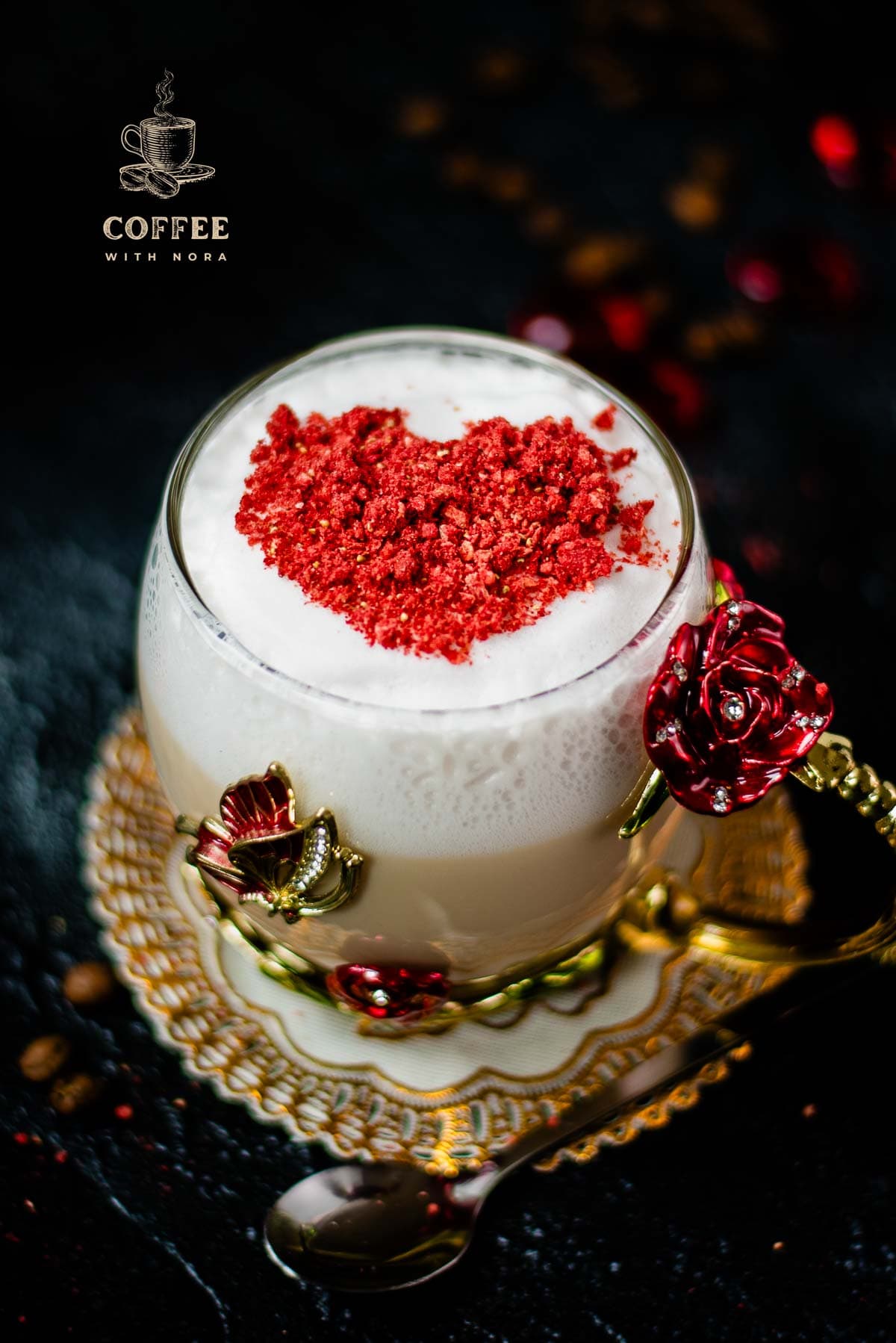 Gorgeous hot strawberry latte, served in a glass mug decorated with roses and butterflies. On top of the coffee is a red heart made from chopped freeze-dried hearts.