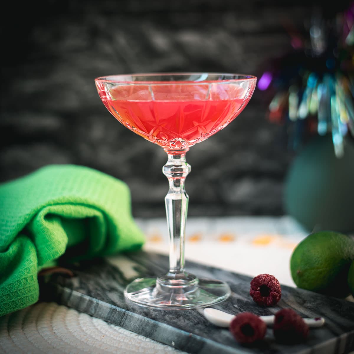 Gorgeous raspberry daiquiri with a vibrant red color placed on marble plate next to three raspberries.