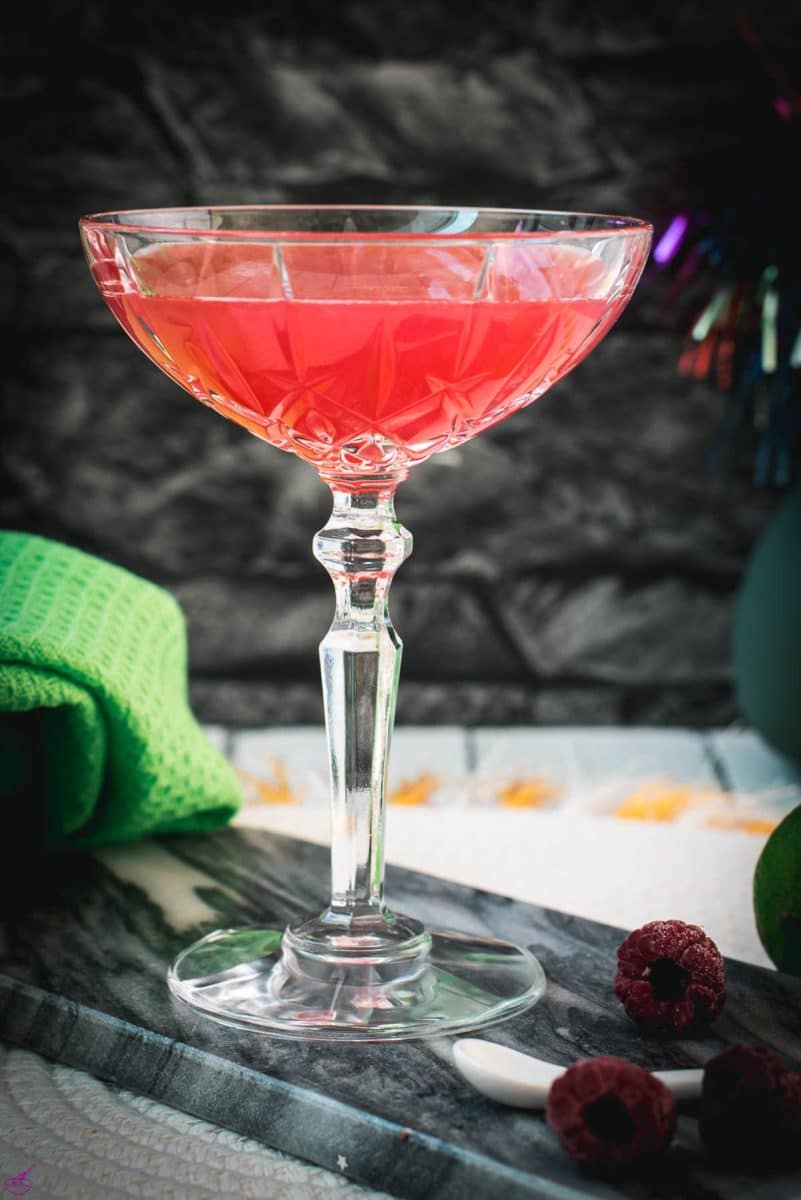 Gorgeous raspberry daiquiri with a vibrant red color placed on marble plate next to three raspberries.