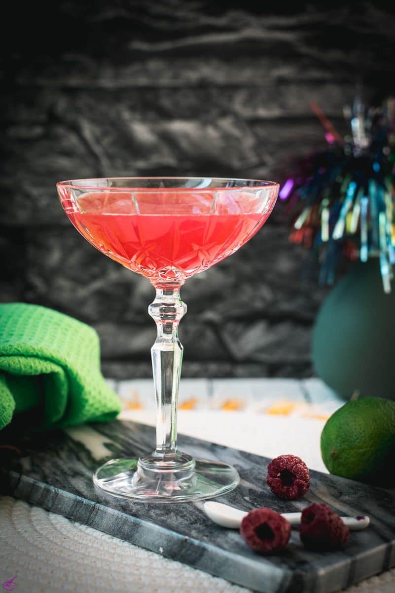 Gorgeous raspberry daiquiri with a vibrant red color placed on marble plate next to three raspberries.