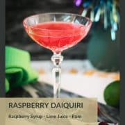 Gorgeous raspberry daiquiri with a vibrant red color placed on marble plate next to three raspberries.