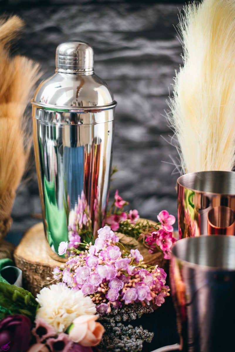 Cobbler shaker placed on wooden slice next to flowers.