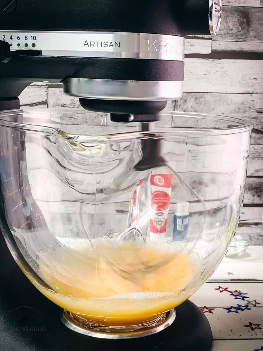 Kitchen machine with a whisk attachment, mixes yellow cake batter.