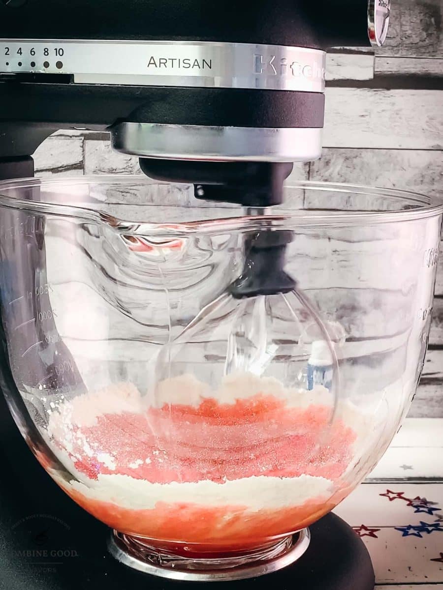 Kitchen machine with a whisk attachment, mixes red cake batter.