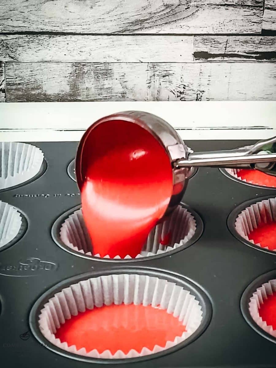 Ice cream scoop pours red cake batter into the muffin tin.