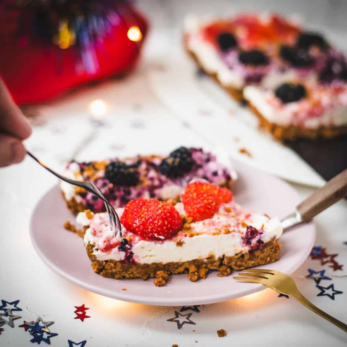 Delicious no-bake 4th of July fruit tart slices, placed on pink plate and two forks that wanna grab a bite.